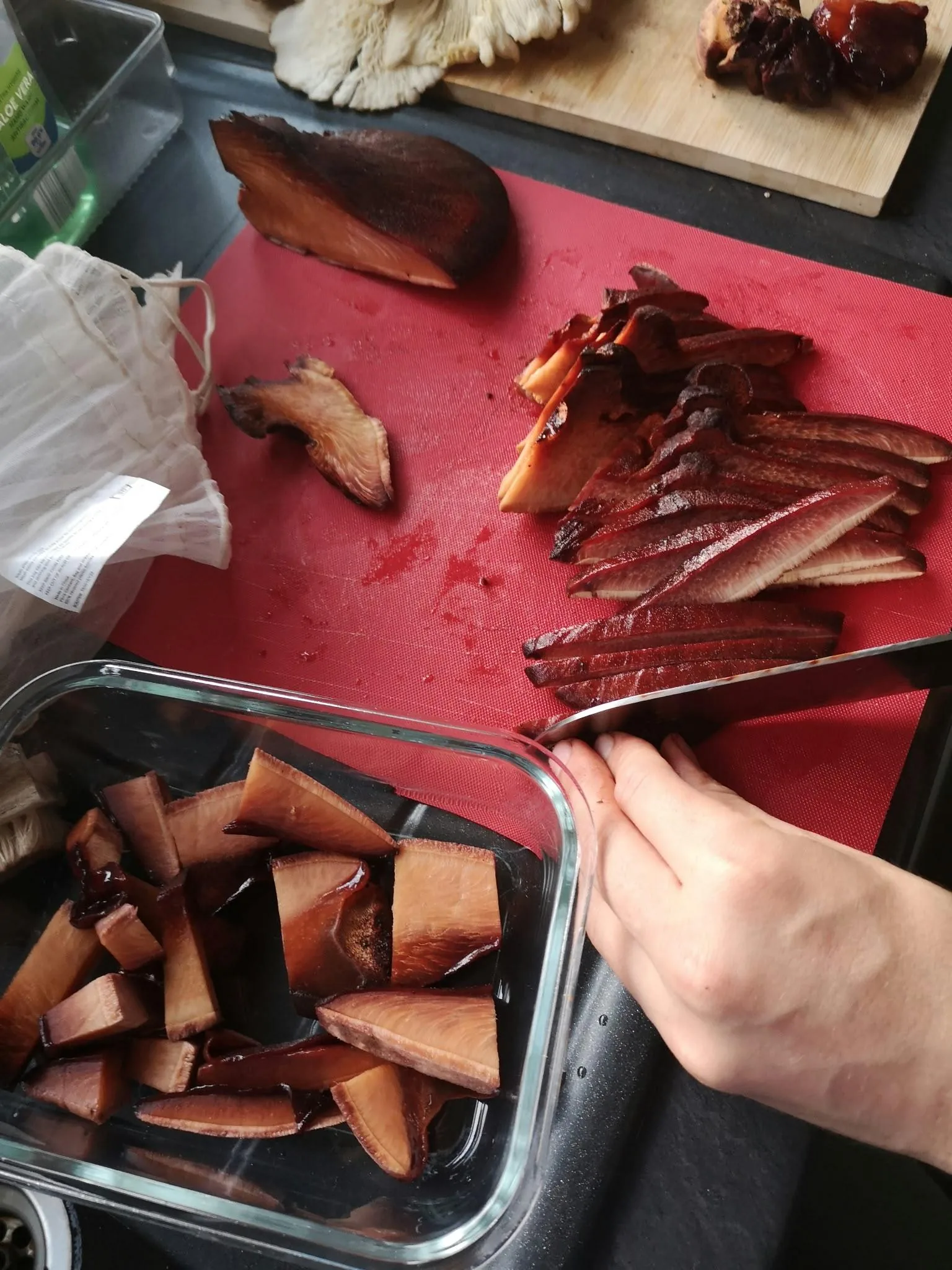 Beefsteak mushroom sliced into thick and thin strips on a red chopping board, with chunks in a glass tub