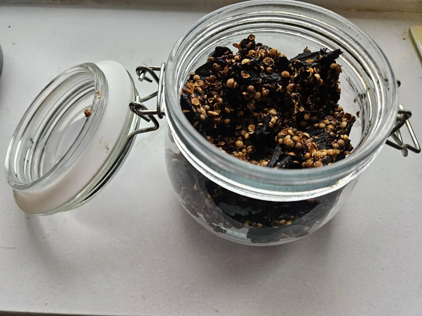 An open clip-top jar of finished beefsteak mushroom biltong with the lid resting beside it